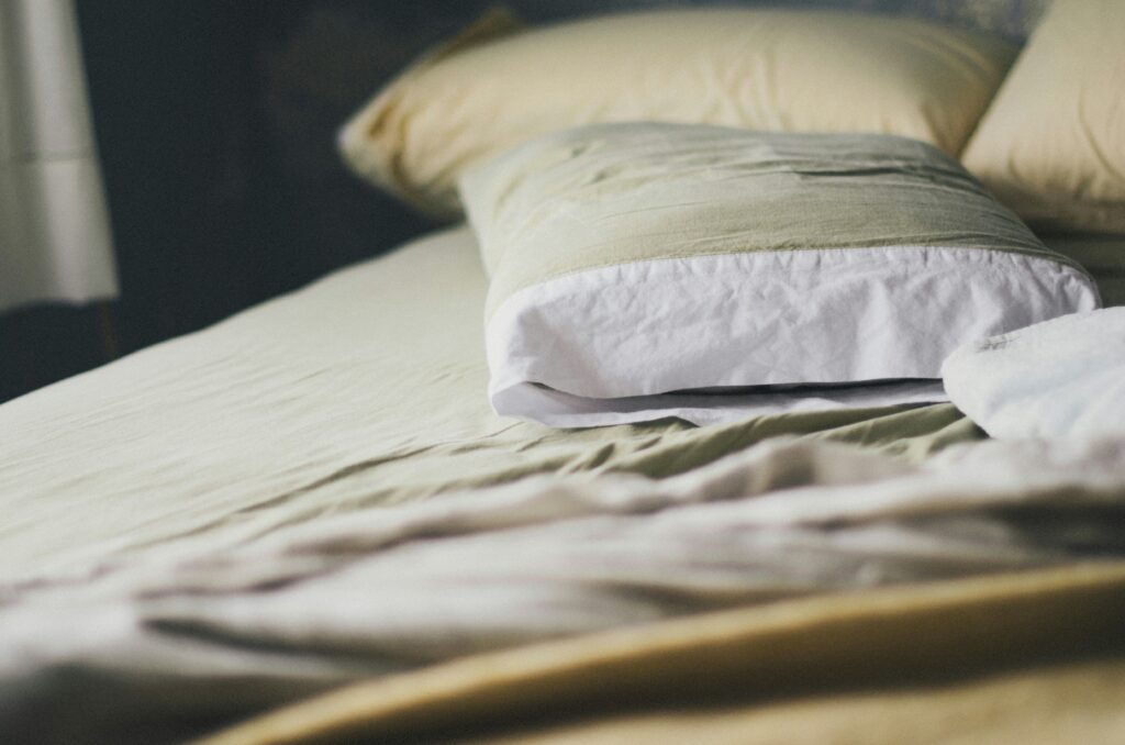 Close-up view of a neatly made bed with beige sheets and a pillow covered in a light green and white pillowcase, creating a calm and cozy bedroom atmosphere.