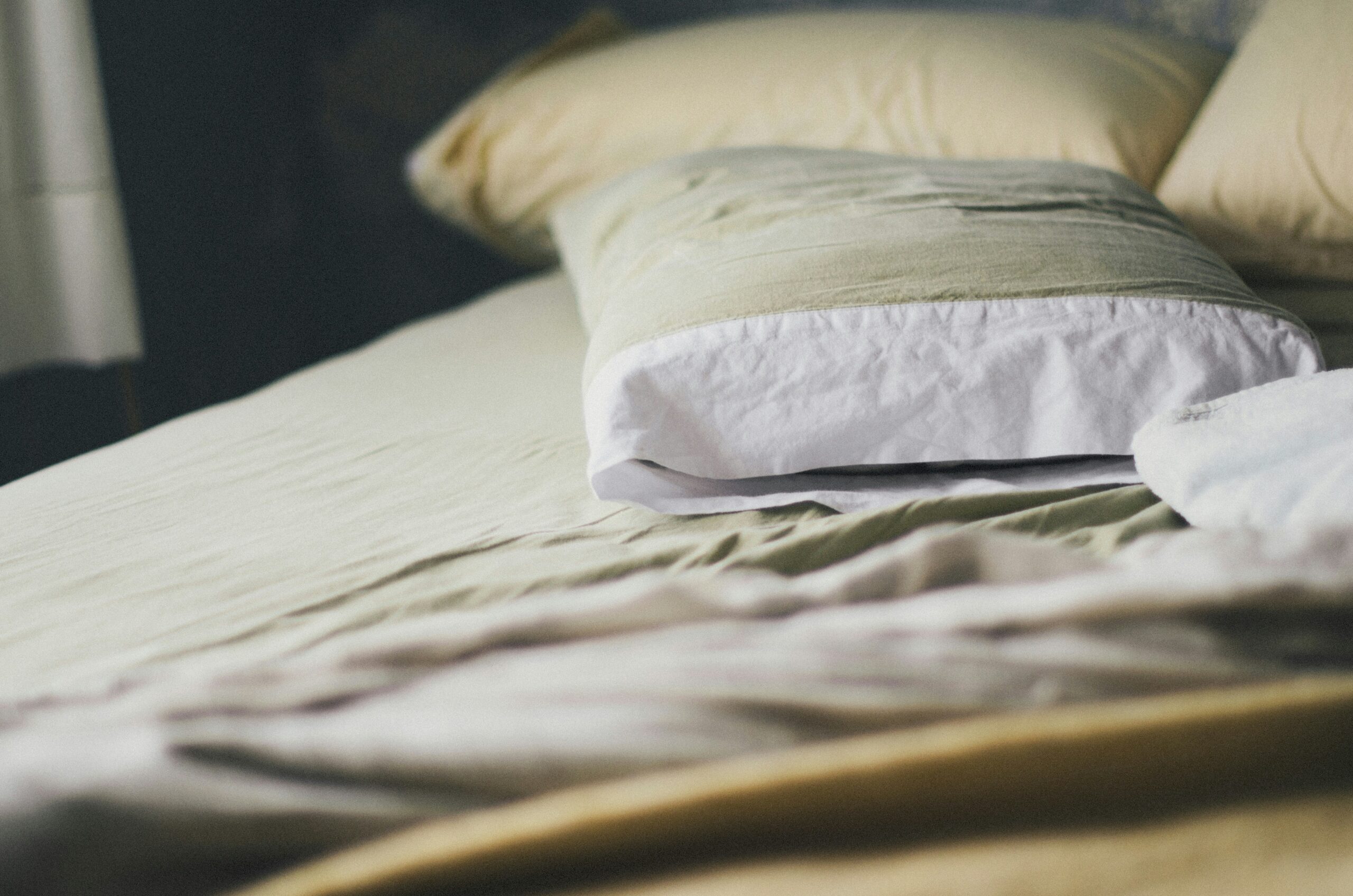 Close-up view of a neatly made bed with beige sheets and a pillow covered in a light green and white pillowcase, creating a calm and cozy bedroom atmosphere.