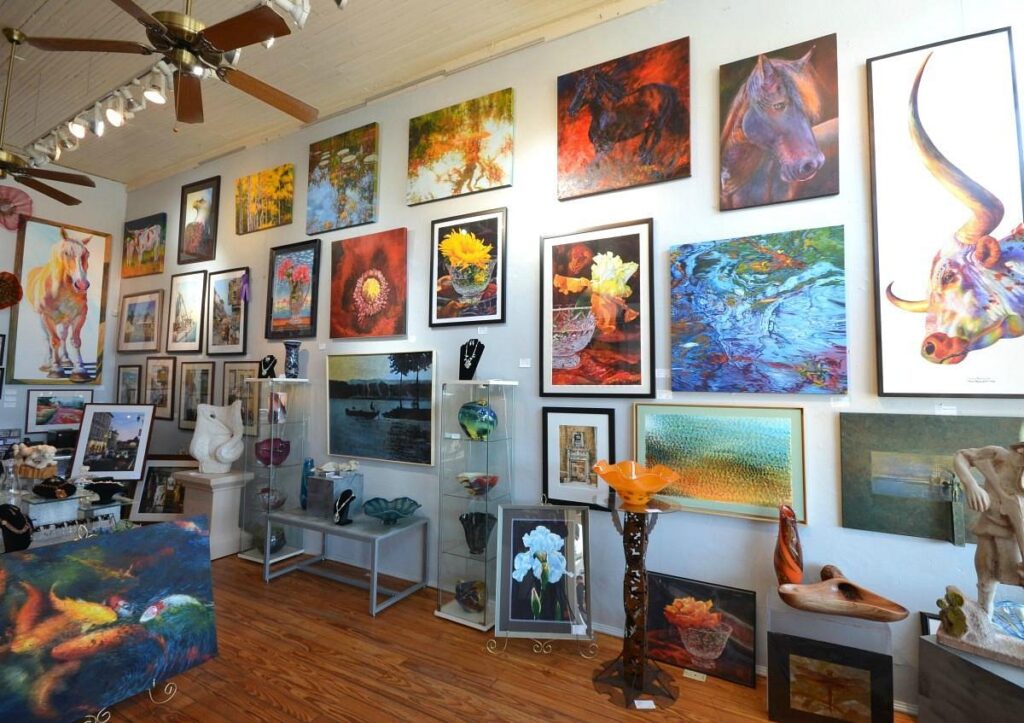 Art gallery interior showcasing colorful contemporary paintings and sculptures, featuring nature-inspired artworks, animal portraits, and glass decor pieces on display.